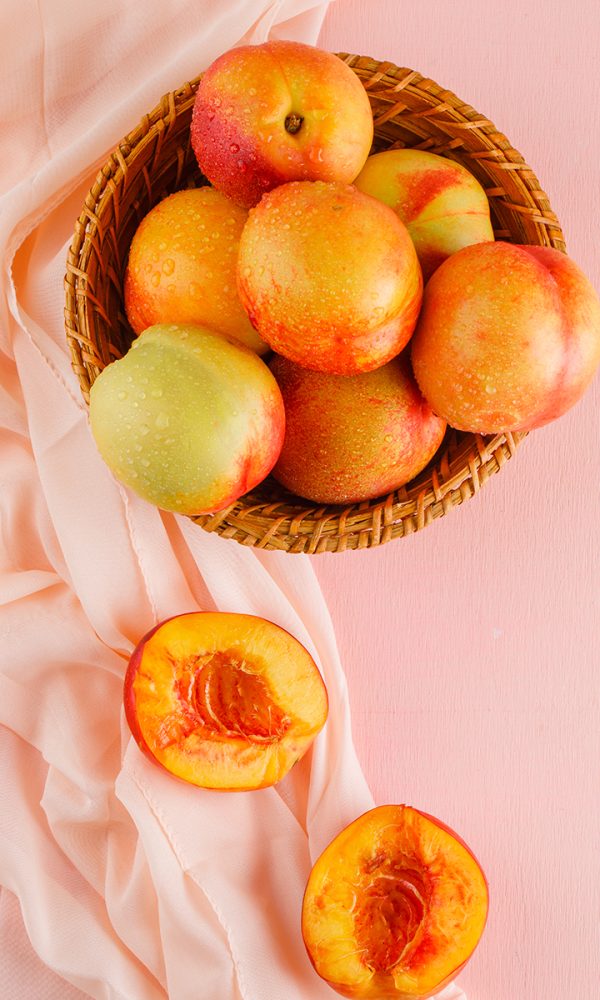 Nectarines basket top view pink textile surface 600x1000