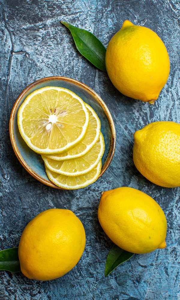 Vertical view whole cut fresh lemons with leaves left side dark background 600x1000