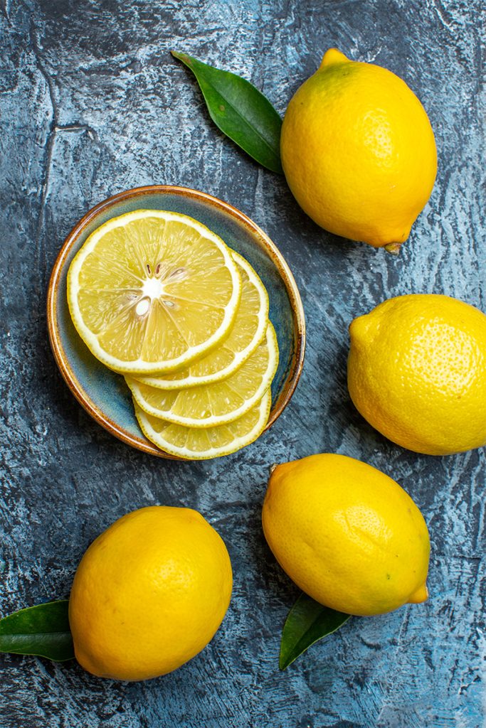Vertical view whole cut fresh lemons with leaves left side dark background 683x1024