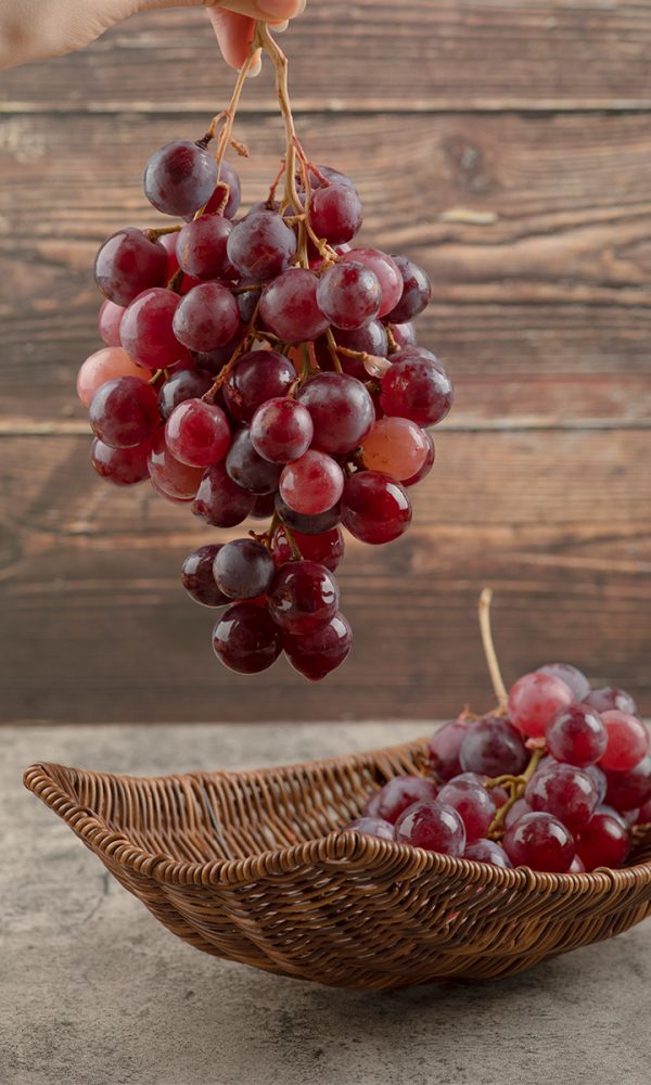 Woman hand holding cluster red grapes wooden background 600x1000
