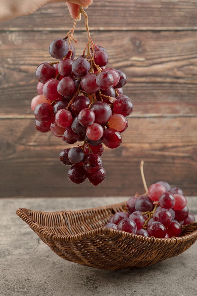 Woman hand holding cluster red grapes wooden background 683x1024